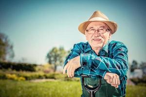 ritratto di un giardiniere anziano in piedi in un giardino con una pala. foto