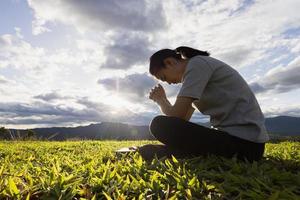 donna che prega per ringraziare Dio pregando con le mani unite per pensare a un dio amorevole, lodiamo Dio con un bagliore di luce nella natura verde. foto