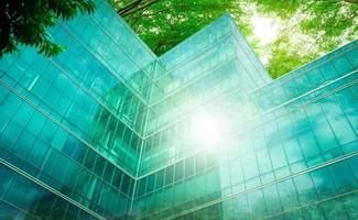 edificio ecologico nella città moderna. rami di alberi verdi con foglie e un edificio in vetro sostenibile per ridurre il calore e l'anidride carbonica. edificio per uffici con ambiente verde. vai concetto verde. foto