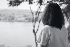 il punto di vista posteriore della donna asiatica triste nel parco guarda la vista del lago. donna depressa. concetto di salute mentale. preoccupazione e ansia donna. vita infelice. persona sola e sola. fotografia in bianco e nero. foto