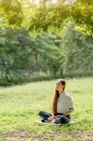 donna asiatica che indossa un abito bianco meditazione nel parco all'alba in primavera o in estate. foto