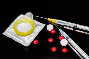 i medicinali bianchi e rossi con una siringa di plastica e un preservativo isolano su sfondo nero. campione di ciò che ha causato l'infezione da hiv. e il preservativo serve a prevenire l'infezione. foto