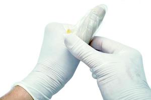 mani del medico in guanto medico in lattice blu che mostra una dimostrazione dell'uso del preservativo dal pollice invece dei genitali maschili su sfondo bianco. foto