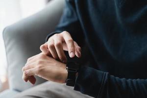 mani dell'uomo che toccano lo schermo dell'orologio intelligente seduto sul divano di casa. foto