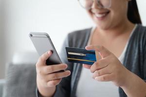 donna in possesso di carta di credito e utilizzando smartphone per lo shopping online, internet banking, e-commerce, spendere soldi. foto