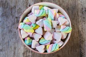 twist e cuore di marshmallow multicolore in una ciotola su uno sfondo di legno. copia spazio sullo sfondo e la trama foto