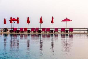 ombrellone rosso e sedie da piscina all'alba intorno alla piscina all'aperto. foto