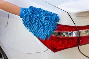 mano donna con tessuto in microfibra blu lavaggio auto moderna fanale posteriore o pulizia automobile. concetto di autolavaggio foto