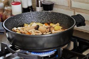 le carote con funghi e patate vengono fritte in padella sul fornello a gas per fare lo spezzatino di pesce con le verdure. ricetta passo passo foto