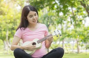 donna asiatica che suona l'ukulele e sorride felicemente nel parco. foto