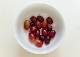 alcune uve rosse in una ciotola bianca di porezellan piccola ciotola di vetro su un tavolo bianco - vista dall'alto foto