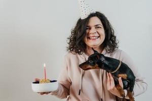 ragazza felice che dà una torta fatta in casa al suo cane, al chiuso foto