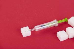 zollette di zucchero bianco e siringa da insulina su sfondo rosso. copia spazio. foto
