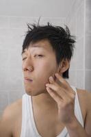 Metà di uomo adulto asiatico che esamina il suo fronte in bagno