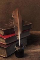 libri antichi, pergamene, penna piuma e calamaio sul tavolo di legno foto