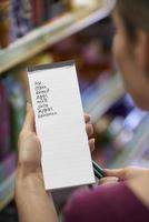 donna che legge la lista della spesa in un supermercato foto