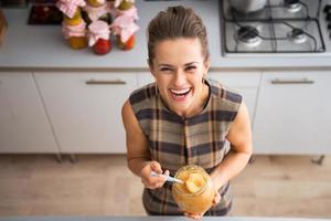 Ritratto di giovane casalinga felice tenendo il barattolo con marmellata di mele foto