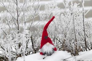 un piccolo giocattolo seduto nella neve in abiti rossi foto