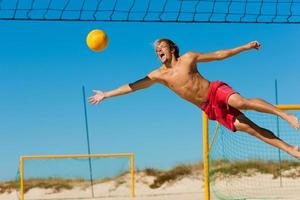 uomo in spiaggia che salta in aria mentre cerca di ottenere la pallavolo