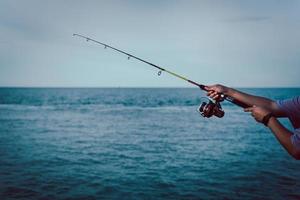 primo piano della ruota della canna da pesca, uomo che pesca dalla barca nel mare foto