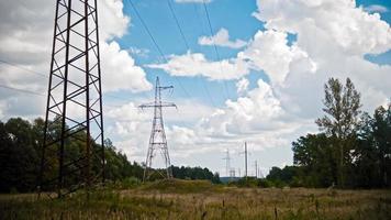 timelapse wide shot di linee elettriche e tralicci ad alta tensione su un campo in campagna in estate. foto