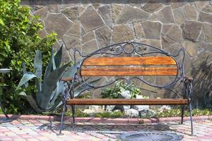panca di legno vuota in una soleggiata giornata estiva con un cactus sullo sfondo di un muro di pietra. stile mediterraneo. foto