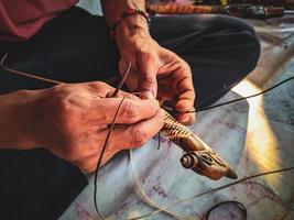 primo piano della mano di un uomo che fa un cerchio di rattan su un manico di mandau foto