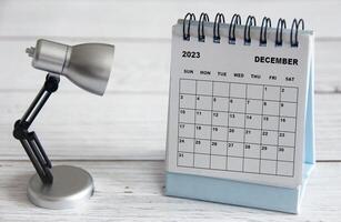 dicembre 2023 calendario da tavolo bianco con lampada da tavolo su tavola di legno. foto