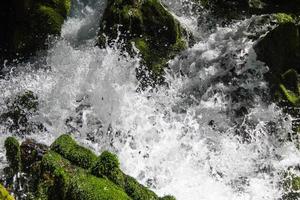 foto ravvicinata di una cascata fresca e pulita circondata da rocce ricoperte di muschio verde