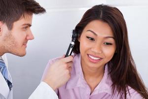medico che esamina l'orecchio del paziente con otoscopio foto