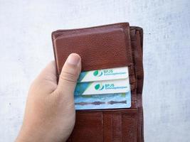 surabaya, jawa timur, indonesia, 2022 - un uomo con in mano un portafoglio contenente una carta bpjs e ktp foto