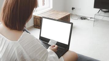 una donna in possesso di una carta di credito, che sta pagando online, su un laptop, seduta sul divano in soggiorno, a casa con un tracciato di ritaglio. il concetto di shopping online.taccuino con schermo bianco per mockup foto