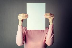 donna anonima che copre il viso con un foglio di carta bianca foto