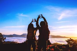 amante donne e uomini asiatici viaggiano rilassarsi durante le vacanze. alzati per l'alba sulla montagna, felice luna di miele, ha alzato la mano per formare una forma di cuore. foto