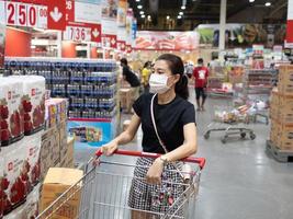 donna che indossa una maschera protettiva monouso per la spesa al supermercato durante l'epidemia di polmonite da coronavirus foto