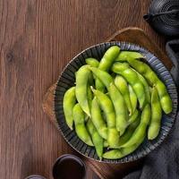 edamame bollito fresco cotto in un piatto sul vassoio di legno e sullo sfondo del tavolo, concetto di cibo proteico sano. foto