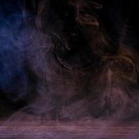 immagine concettuale di fumo multicolore isolato su sfondo nero scuro e tavolo in legno. foto