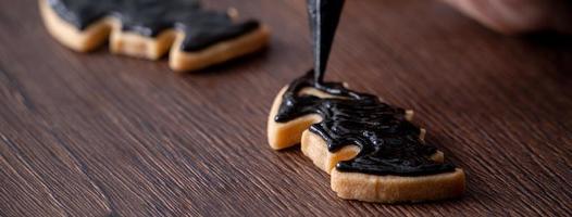 primo piano di decorare simpatici biscotti di zucchero di pipistrello di halloween con glassa. foto