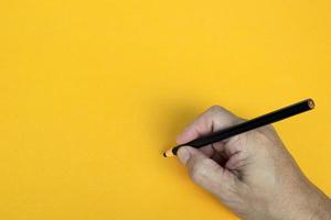 la mano maschile scrive a matita nera su sfondo giallo. copia spazio. foto