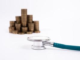 stetoscopio sulla pila di monete, su sfondo bianco. soldi per l'assistenza sanitaria, aiuti finanziari, concetto foto
