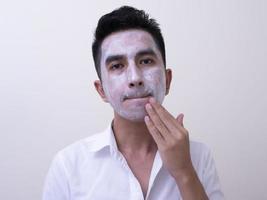 bel giovane asiatico che applica crema sul viso con faccina sorridente, concetto di cura della pelle foto