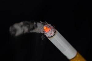 sigaretta accesa con fumo su sfondo nero foto