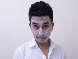 bel giovane asiatico che applica crema sul viso con faccina sorridente, concetto di cura della pelle