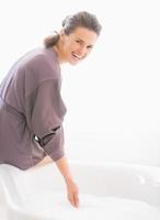 giovane donna felice che controlla la temperatura dell'acqua in vasca