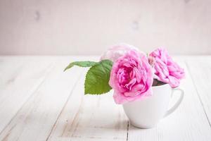 rose da tè rosa su un fondo di legno bianco