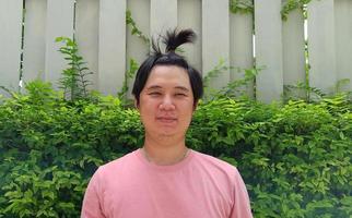 primo piano di un bel ragazzo asiatico hipster barbuto con i capelli in panino, in camicia rosa, sorriso felice, in posa per una foto. foto