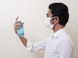 un uomo che indossa una maschera che attualmente usa gel alcolico per lavarsi le mani foto