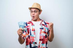 giovane uomo asiatico che mostra un'espressione facciale eccitata mentre tiene i soldi foto