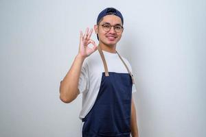 giovane bell'uomo barista che indossa il grembiule sorridente e facendo segno ok con le dita, eccellente simbolo foto