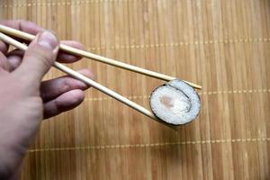 preso con le bacchette sushi con tonno da mangiare. delizioso involtino di pesce. rotolo di sushi di riso su una stuoia. foto